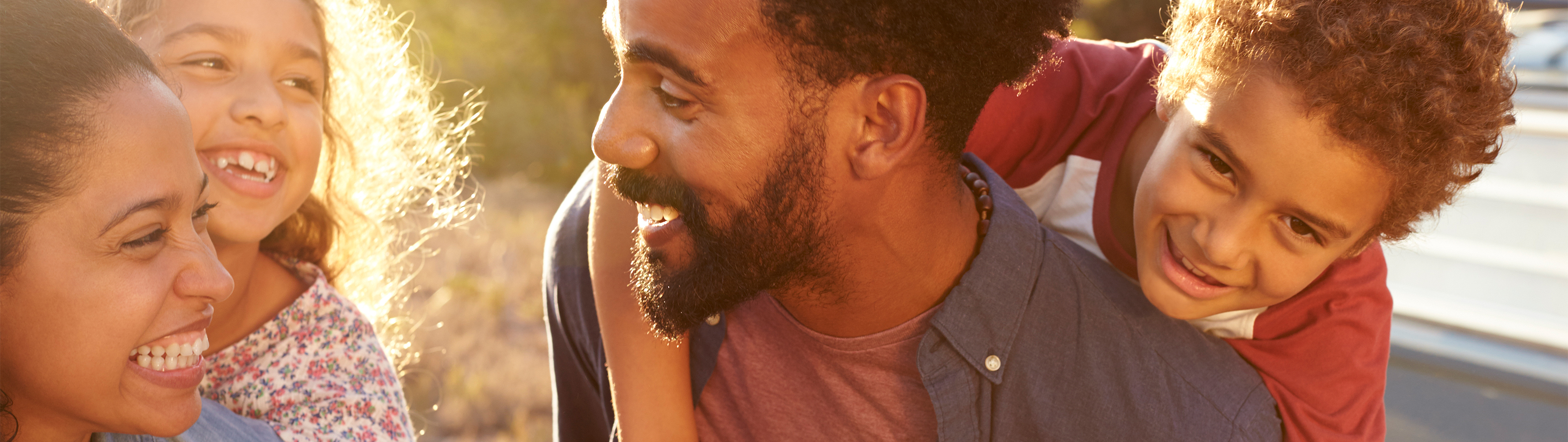 A father and son stand smiling in their driveway. The father has his arm on the son's shoulder. The son is holding a basketball, and a basketball hoop is shown in the background.